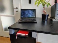 a laptop computer sitting on top of a wooden desk next to a potted plant