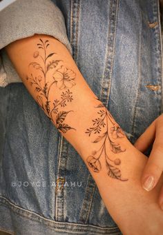 a woman's arm with flowers on it and leaves in the middle, while she is wearing a denim jacket