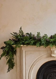 a mantel with pine cones and greenery on top, next to a fireplace