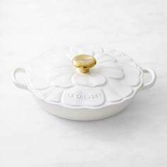 a white casserole dish with a gold lid on a marble countertop in the shape of a flower