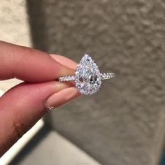 a woman's hand holding an engagement ring with a pear shaped diamond on it