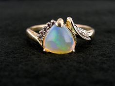 "Polished to perfection and filled with glitters of light in every shade of the rainbow, this gorgeous opal gemstone shines with fire from each of its three facets. We love the nearly heart shaped profile of this trillion cut stone, and the slightly asymetrical flow it gives the gold and diamond setting! Metal: 14K Yellow Gold Gem: Opal 1.53 Carats Gem Measurements: 8.6 mm, Trillion Cut Accents: 8 Diamonds totaling .10 Carat Ring Size: 11 Marks: \"14K\" Stamped on the inside band SKU #: VW4YPF-N Opal Ring With Diamond Accents For Gift, Gift Opal Ring With Diamond Accents, Elegant Multicolor Opal Jewelry, Iridescent Opal Jewelry For Anniversary, Multicolor Opal Jewelry For Anniversary, Yellow Gold Opal Ring With Diamond Accents For Gift, Elegant Opal Heart Cut Jewelry, Dazzling Opal Gemstone Ring Gift, Elegant Iridescent Opal Ring With Cabochon