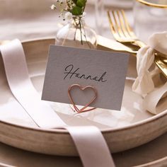 a place card with a heart on it sitting on a plate next to a fork and knife