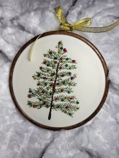 a cross stitch christmas tree ornament hanging from a wooden hoop on white fur