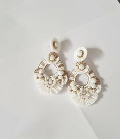 "Boho White and Gold Raffia embellished statement medium size earrings. The earring is hand embroidered using various elements like Raffia, handmade silk pompoms, faux pearl, glass beads, and much more material. This lightweight medium size Raffia white with gold accent earring is a piece of perfect wedding jewelry. The Earrings measure about approx. 2.75\" long and 2.10\" wide. PS: Carnation jewelry is handmade & handcrafted in India hence there is a possibility of a slight or small imperfe Elegant Summer Chandelier Earrings With Tassels, Elegant Summer Tassel Chandelier Earrings, Elegant Gold Tassel Earrings For Beach, Elegant Beaded Earrings For Summer Wedding, Bohemian White Earrings For Beach, Bohemian White Beaded Earrings, White Beaded Tassel Drop Earrings, White Bohemian Beaded Earrings With Tassels, White Beaded Earrings For Summer