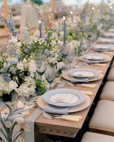 the table is set with blue and white plates, silverware, and floral centerpieces