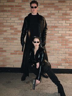 a man and woman dressed in black standing next to each other with sunglasses on their faces