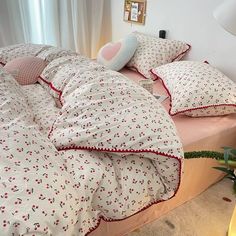 a bed with white and red sheets and pillows on top of it next to a night stand