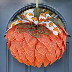 an orange mesh wreath hanging on the front door of a house with leaves and acorns