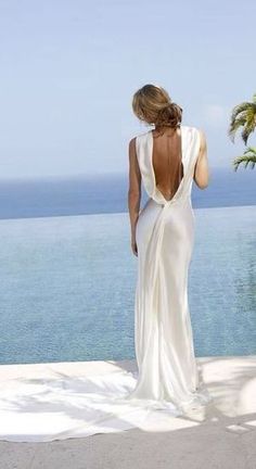 the back of a woman in a white dress looking out at the ocean from her balcony