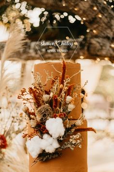 a brown wedding cake with dried flowers and greenery on top is surrounded by lights