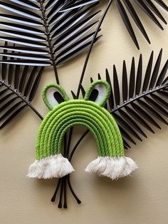 a green frog made out of rope and some black palm leaves on the side of a wall