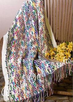 a colorful blanket sitting on top of a wooden chair next to a vase with flowers