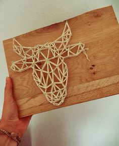 a person is holding a wooden board with string art on it that looks like a deer head