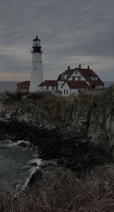 a light house sitting on top of a rocky cliff next to the ocean under a cloudy sky