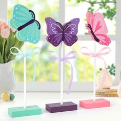 three different colored butterflies on sticks in front of a window