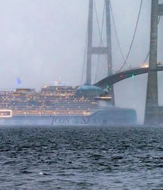 a large cruise ship passing under a bridge in the foggy water with lights on