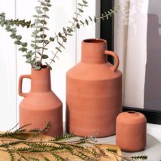 three clay vases sitting on top of a table next to a potted plant