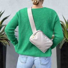 a woman wearing a green sweater and jeans is holding a gray purse in her hand