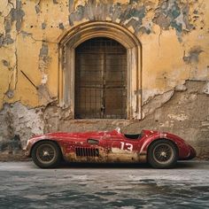 an old red sports car is parked in front of a building with peeling paint on it