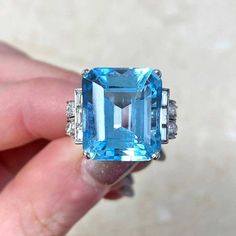 This remarkable engagement ring with a 10.72 carat emerald cut aquamarine is prong-set. The center stone is surrounded by two baguette-cut diamonds. Curved and set with a variety of old European cut diamonds on the shoulders of the ring. This ring contains approx 0.96 carats of diamonds in total and is handcrafted with a geometric openwork under-gallery in platinum. ✦ GEMSTONE SPECIFICATIONS: Center Gemstone: Aquamarine Gemstone Cut: Emerald Cut Total Aquamarine Weight: Approx. 10.72 Carats Tota Luxury Platinum Topaz Gemstone Ring, Gia Certified Octagon Sapphire Ring, Luxury Style, Gia Certified Octagon Sapphire Luxury Ring, Luxury Gia Certified Octagon Sapphire Ring, Luxury Octagon Sapphire Ring In Platinum, Luxury Platinum Octagon Sapphire Ring, Luxury Octagon Sapphire Platinum Ring, Luxury Platinum Topaz Ring With Accent Stones, Emerald Cut Platinum Gemstones In White Gold