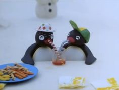 two penguin figurines sitting next to each other on a table with food and drinks