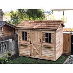 a small wooden shed sitting in the grass next to a fence and some other wood buildings