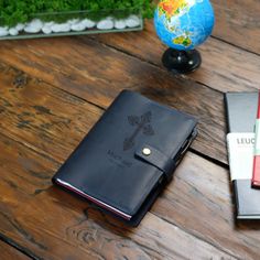 a leather notebook sitting on top of a wooden table next to a globe and pen