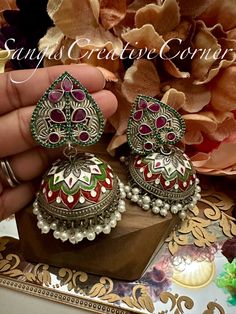 Looking for a one of a kind meenakari handpainted STATEMENT set of jhumka style earrings and doesn't hurt your ears, look no further! This lightweight  brass-based textured silver tone finish jhumka style earrings has a very contemporary style with multi colors painted work encompassed with pearl embellishments at the bottom of earrings. There are two variations to this piece: One that has green/red stones while the other has a clear stones.  The combination of the stone work with a silver tone painted brass-based metal finish will surely make you get those well-deserved jaw-dropping attention. It's the right balance you need to make a statement but not over the top.     Highlights of the piece: ** Dangled full jhumka style earrings with height: 3.25 inch ** Pushback in the back for the ea Multicolor Kundan Danglers With Intricate Design, Multicolor Intricate Earrings For Navratri, Traditional Earrings With Artistic Design For Festivals, Multicolor Temple Jewelry Danglers With Intricate Design, Traditional Artistic Design Earrings For Festivals, Kundan Jhumkas With Motifs For Gifts, Kundan Jhumkas With Motifs As A Gift, Multicolor Round Chandbalis With Intricate Design, Temple Jewelry Cutdana Jhumkas As Gift