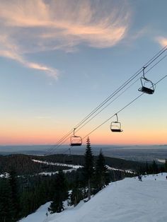 the ski lift is going over the snow covered hill at sunset with people skiing below