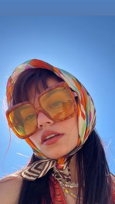 a woman wearing sunglasses and a scarf on her head with the sky in the background