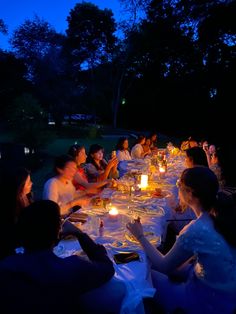 a group of people sitting around a table with candles in their hands at night time