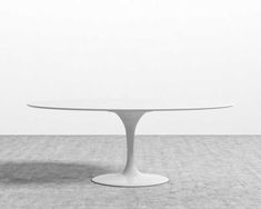 an oval white table sitting on top of a cement floor in front of a wall