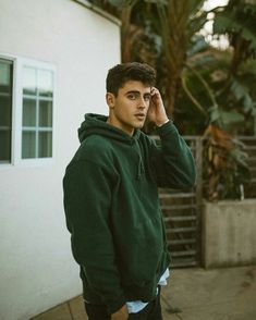 a young man in a green hoodie is holding his hand to his ear and looking at the camera