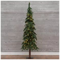 a small christmas tree with lights on it in front of a wooden wall and floor