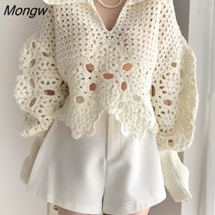 a woman is wearing white shorts and a crochet jacket with pearls on it