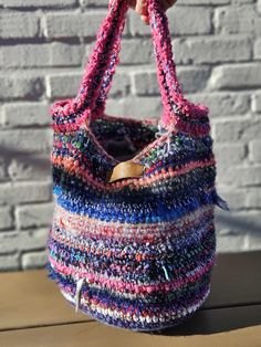 a hand holding a multicolored knitted bag on top of a wooden table