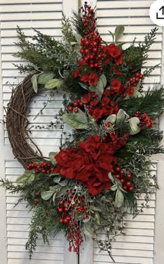 a wreath with red flowers and greenery hanging on a door