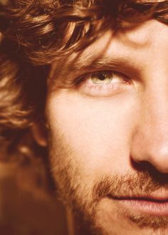 a close up of a man with curly hair and blue eyes looking at the camera