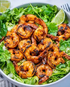 grilled shrimp and lettuce in a bowl with lime wedges on the side