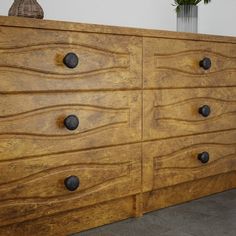 a large wooden dresser with black knobs on it's doors and drawers, next to a potted plant