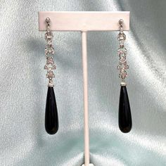 A striking pair of antique platinum hanging earrings. These earrings feature old European cut diamonds with Art Deco links. Set on top are are bezel-set diamonds. Set below the intricate diamond design are additional bezel-set diamonds that are attached to long polished onyx drops by a platinum link allowing movement. The total approximate weight of the diamonds is 1 carat. These earrings are handcrafted in platinum.
The measurements of the earrings from the top bezel diamond to the bottom onyx Luxury Art Deco Diamond Earrings As Gift, Luxury Art Deco Diamond Earrings With Brilliant Cut, Art Deco Diamond Earrings Hallmarked, Chandler Earrings, Bezel Set Diamond Earrings, Luxury Black Art Deco Earrings, Vintage Diamond Earrings, Classic Black Diamond-cut Earrings, Estate Diamond Jewelry