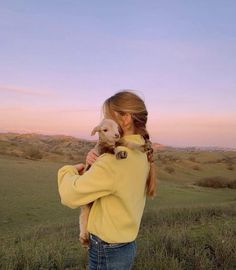 a woman holding a baby goat in her arms while standing on top of a lush green field