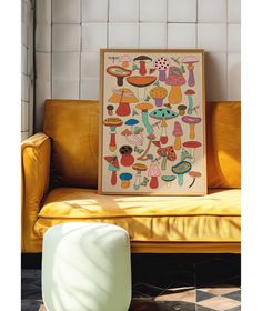 a yellow couch sitting next to a painting on top of a wooden frame in front of a white tiled wall