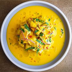 a white bowl filled with yellow soup on top of a wooden table