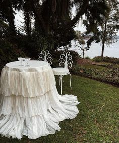 two white chairs sitting on top of a lush green field next to a table covered in a ruffled cloth