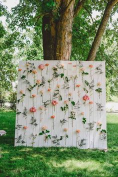 an art piece with flowers on it in front of a tree and some grass, next to a bench