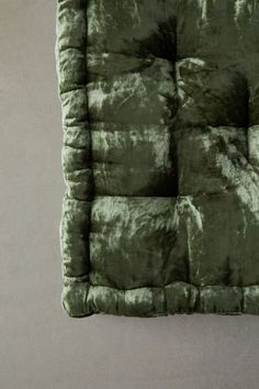 the square cushion is made from green velvet and sits on top of a white floor