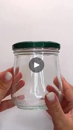 two hands hold a glass jar with a green lid and white nails on the bottom