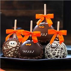 chocolate covered candies with orange bows and eyes on them sitting on a black plate